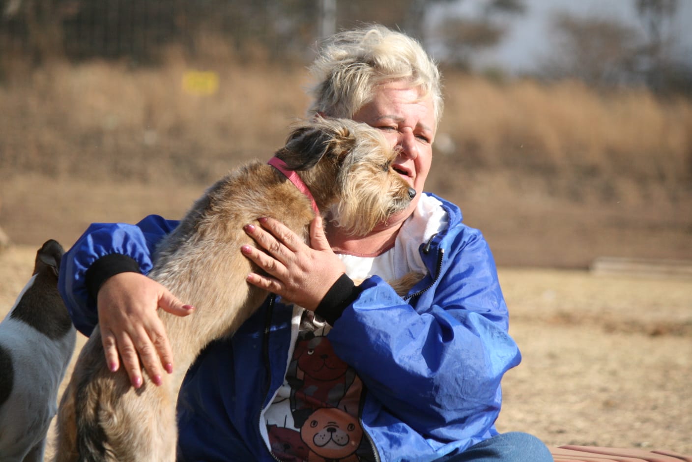 Julie cuddling a terrier that has jumped up into her arms out in the field